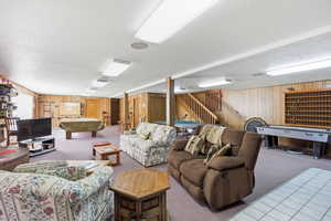 Living room with a textured ceiling, wood walls, pool table, and carpet flooring