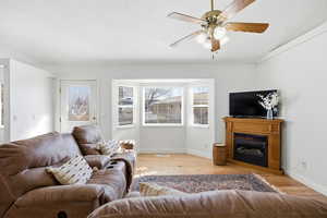 Living area featuring light wood-style floors, a ceiling fan, and a glass covered fireplace
