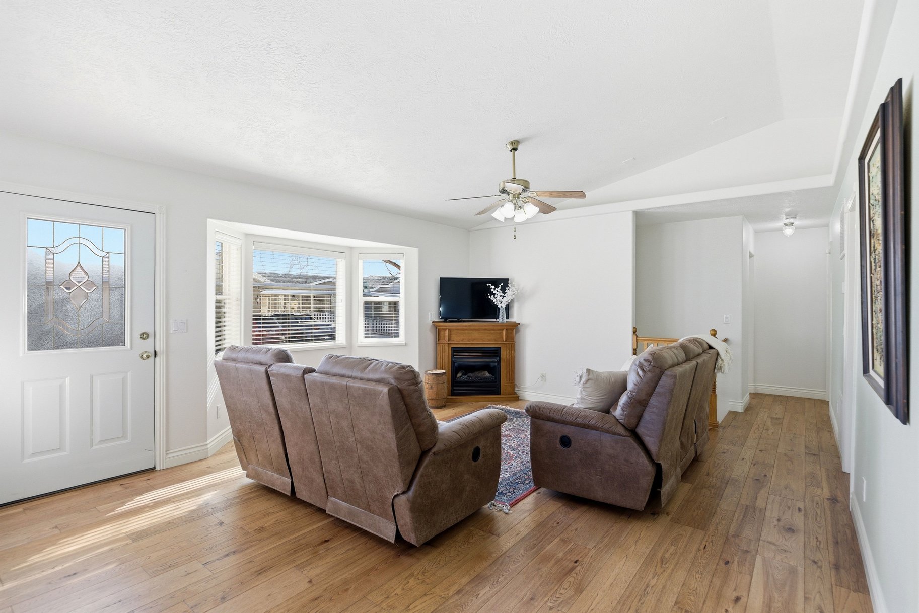 Living room with light wood-style floors, lofted ceiling, ceiling fan, and a glass covered fireplace
