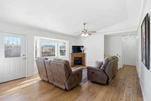 Living room with light wood-style floors, lofted ceiling, ceiling fan, and a glass covered fireplace