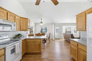 Kitchen featuring white appliances, light wood finished floors, open floor plan, lofted ceiling, and a peninsula