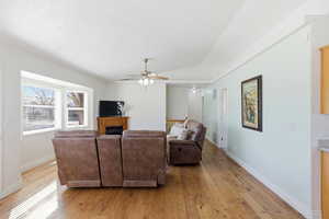 Living room with light wood finished floors, a ceiling fan, a fireplace, and vaulted ceiling