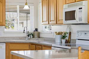 Kitchen featuring white appliances, pendant lighting, and light stone countertops