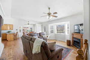 Living room featuring light wood-style flooring, a fireplace, lofted ceiling, and a ceiling fan