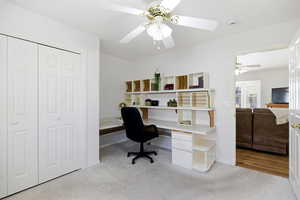 Home office with light carpet, built in desk, and ceiling fan