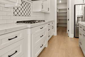 Kitchen with stainless steel appliances, light wood-style flooring, white cabinetry, and light stone countertops