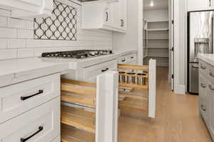 Kitchen with stainless steel appliances, light wood-type flooring, white cabinets, and light stone counters