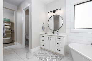 Bathroom with light marble finish floors, a spacious closet, vanity, and a freestanding tub