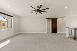 Spare room with a barn door, ceiling fan, light colored carpet, and recessed lighting