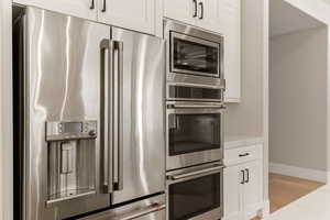 Kitchen featuring stainless steel appliances, white cabinetry, light wood-style flooring, and light stone countertops