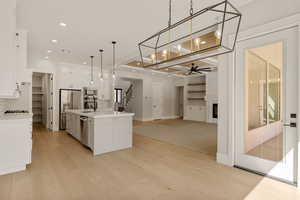Kitchen featuring open floor plan, a kitchen island with sink, stainless steel appliances, white cabinets, and a fireplace
