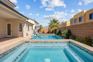View of swimming pool with patio surround, a water slide, a fenced backyard, and an in-ground hot tub