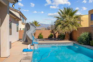 View of pool with a water slide, patio surround, a fenced backyard, and a mountain view