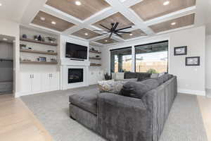 Living room featuring coffered ceiling, recessed lighting, light wood-type flooring, a glass covered fireplace, and ceiling fan