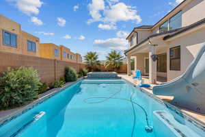Combined pool / hot tub featuring a patio, a fenced backyard, and a water slide