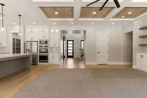 Kitchen with coffered ceiling, stainless steel appliances, hanging light fixtures, a ceiling fan, and light wood-type flooring