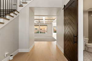 Hall with coffered ceiling, light wood finished floors, a barn door, and recessed lighting