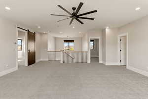Spare room featuring light carpet, a barn door, a ceiling fan, and a chandelier