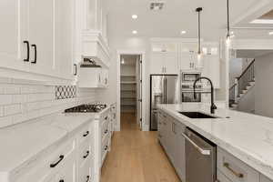 Kitchen featuring light stone countertops, light wood-type flooring, stainless steel appliances, decorative light fixtures, and two tone color scheme
