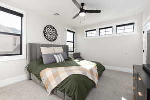 Carpeted bedroom with a ceiling fan and multiple windows