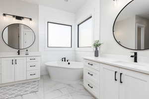 Full bathroom featuring two vanities, a freestanding tub, and light marble finish flooring