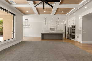 Kitchen featuring open floor plan, coffered ceiling, pendant lighting, stainless steel appliances, and a spacious island