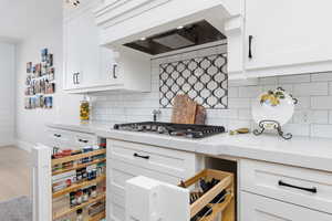 Kitchen with light stone countertops, white cabinets, light wood-type flooring, and stainless steel gas cooktop