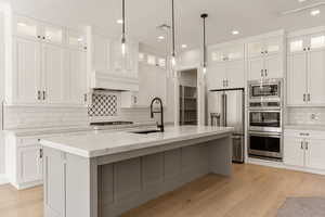 Kitchen featuring glass fronted cabinets, white cabinets, stainless steel appliances, and light stone counters