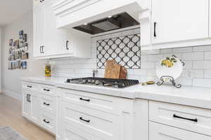 Kitchen featuring light stone countertops, light wood-style flooring, white cabinets, and stainless steel gas cooktop