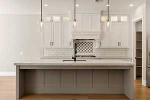 Dual tone kitchen with glass insert cabinets, light stone counters, light wood-type flooring, a kitchen island with sink, and dual tone cabinets