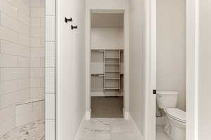 Bathroom with a walk in closet, light marble finish flooring, and a tile shower