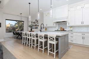 Dual tone kitchen with glass insert cabinets, dual tone cabinets, hanging light fixtures, light stone countertops, and a center island with sink