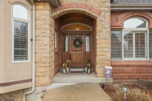 Entrance to property featuring stone siding, brick siding, and roof with shingles