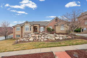 View of front facade featuring a front lawn, brick siding, a shingled roof, and stone siding