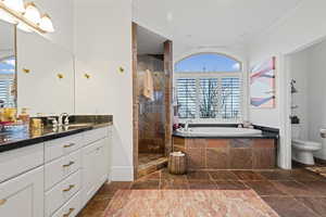 Primary Bathroom featuring a shower stall, a bath, vanity, stone tile floors, and crown molding