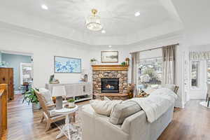 Living room featuring a stone fireplace, wood finished floors, suspended lighting, and a raised ceiling