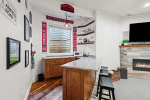 Bar area featuring hanging light fixtures, wood finish cabinetry, light stone countertops, a tile fireplace, and white microwave