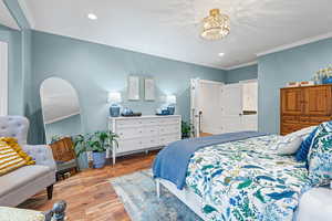 Bedroom featuring crown molding, wood finished floors, a chandelier, and ensuite bath