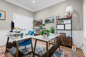 Home office featuring wainscoting, light wood-style floors, crown molding, and a decorative wall