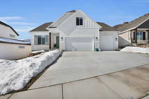 View of front of home with concrete driveway, board and batten siding, stone siding, an attached garage, and a shingled roof