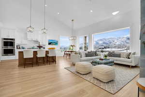 Living room featuring a mountain view, light wood finished floors, vaulted ceiling, and hanging lights