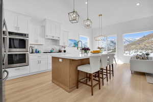 Kitchen featuring stainless steel appliances, light wood finished floors, two tone cabinets, a mountain view, and a breakfast bar area