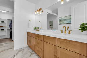 Bathroom featuring double vanity, a spacious closet, and light marble finish flooring