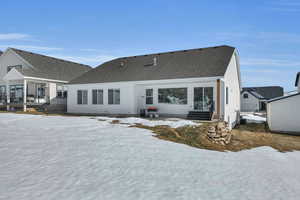 Snow covered house with a shingled roof, a patio, stucco siding, and entry steps
