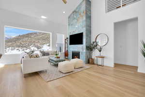 Living area with a mountain view, light wood finished floors, a tiled fireplace, ceiling fan, and lofted ceiling