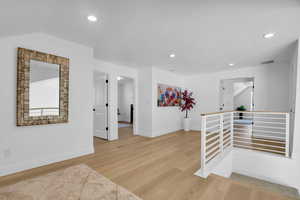 Corridor featuring light wood-type flooring, an upstairs landing, and recessed lighting