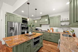 Kitchen with green cabinets, light stone counters, pendant lighting, and dark wood-style floors