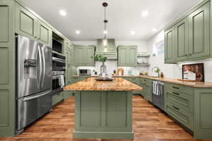 Kitchen featuring green cabinetry, open shelves, stainless steel appliances, light stone countertops, and a kitchen island