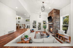 Living room with vaulted ceiling, wood finished floors, a fireplace, and recessed lighting
