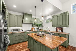 Kitchen with green cabinetry, light stone countertops, decorative light fixtures, a center island, and dark wood finished floors